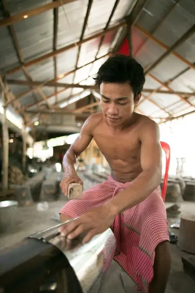 A worker shapes sheet metal during improved cookstove production in Cambodia.