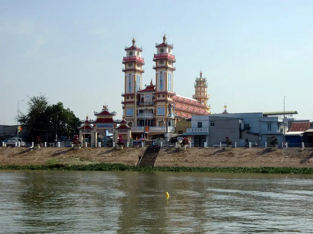 A Cao Dai temple and neighboring buildings behind an embankment on the Tan Chau riverfront.