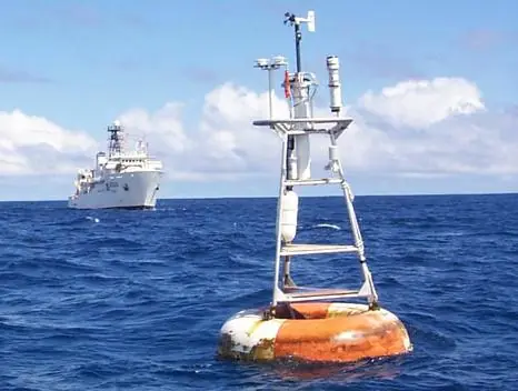 An orange and white TAO/EPIC buoy with weather instruments above the water and a research ship in the background.