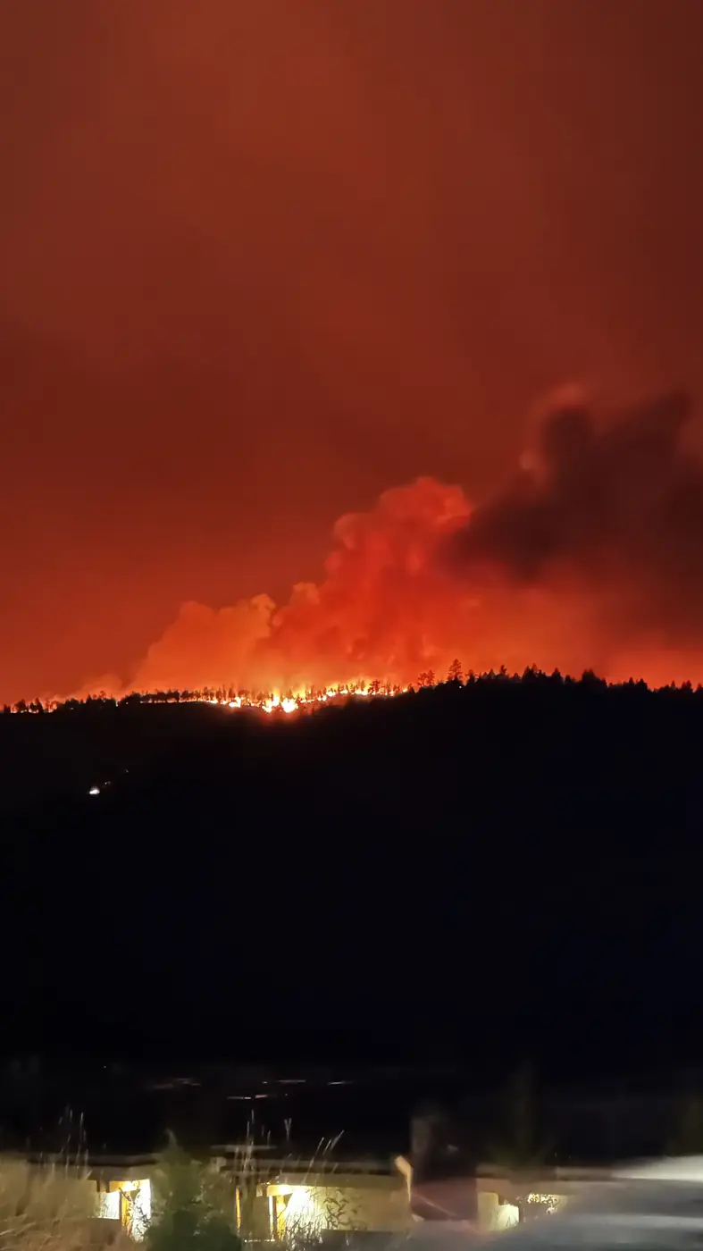Flames burn along a wooded ridge near Kelowna beneath a red, smoke-filled night sky.