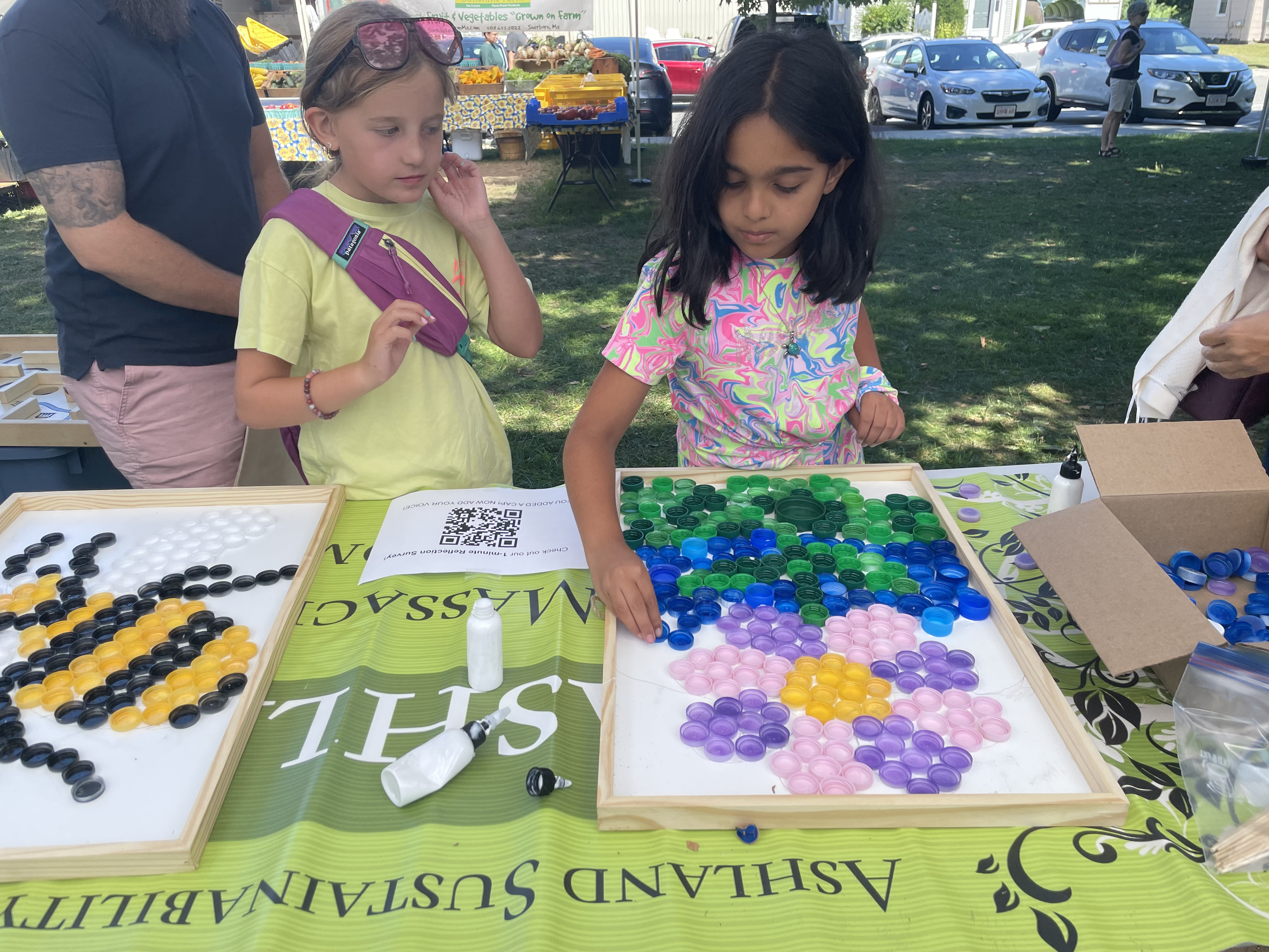 Two children arranging colorful bottle caps into flower mosaics at the Ashland Sustainability booth
