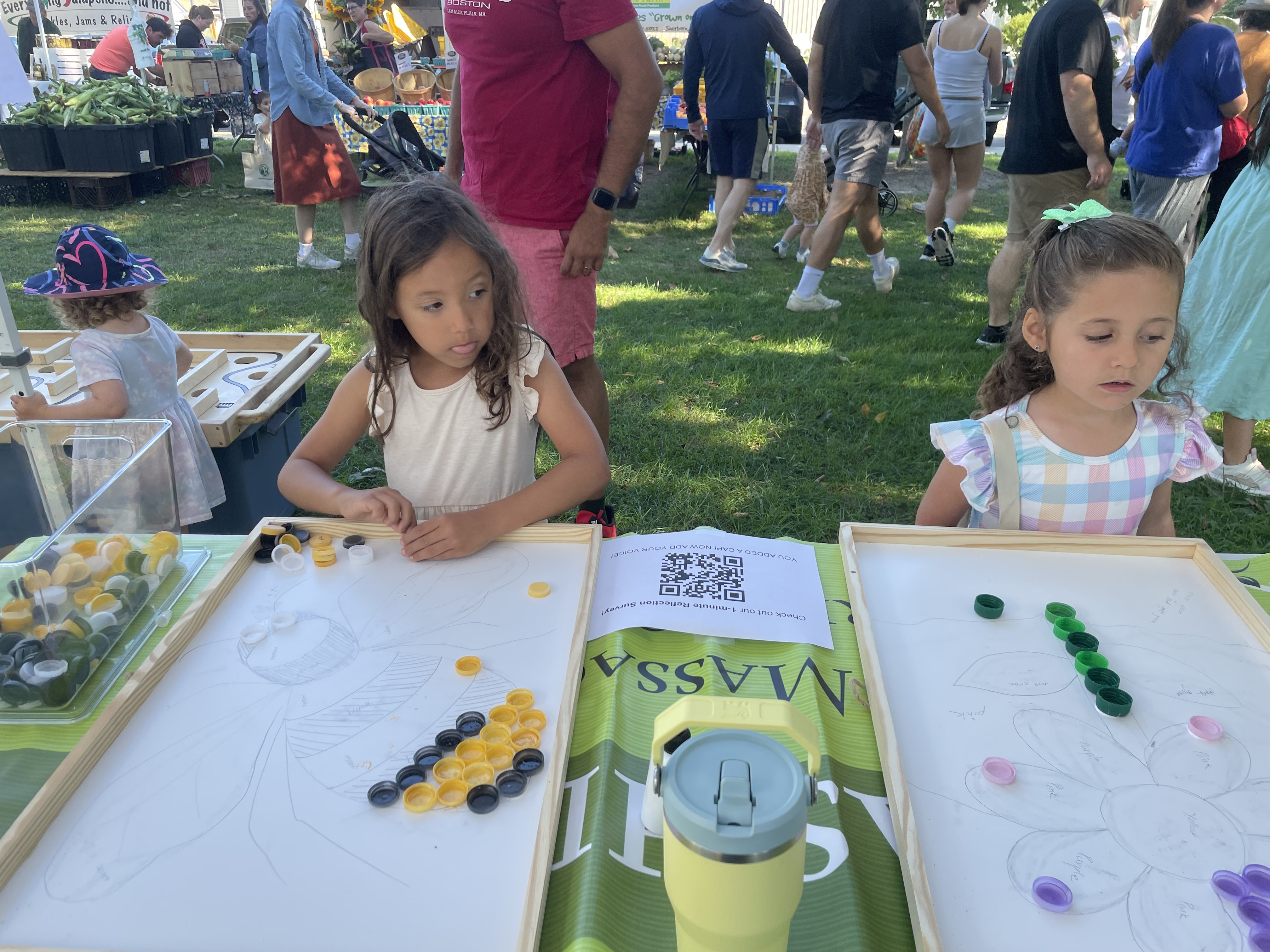 Children filling in hand-drawn flower and bee outlines with yellow and black bottle caps